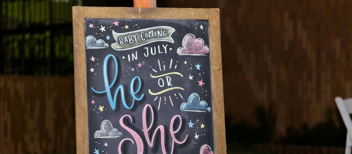 Gender reveal chalkboard reading he or she
