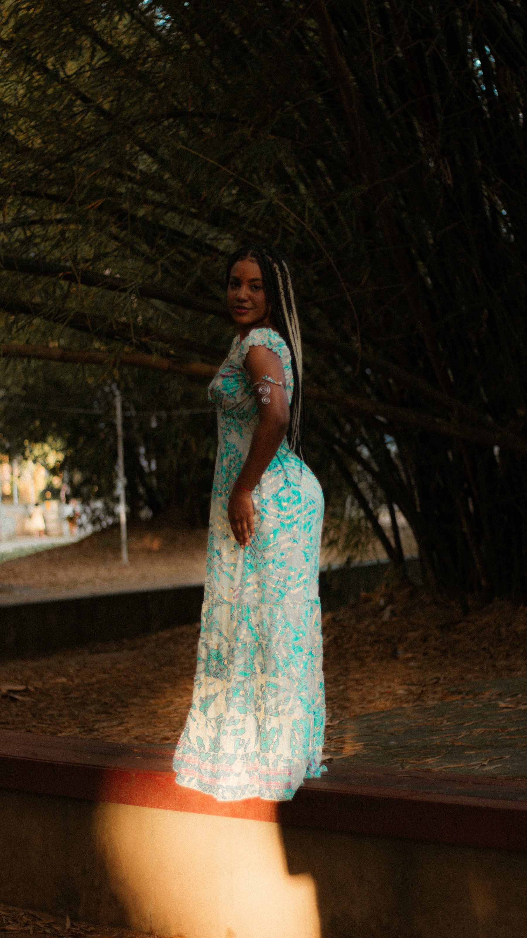 De vestido estampado verde-água sob as árvores do parque, ensaio individual
