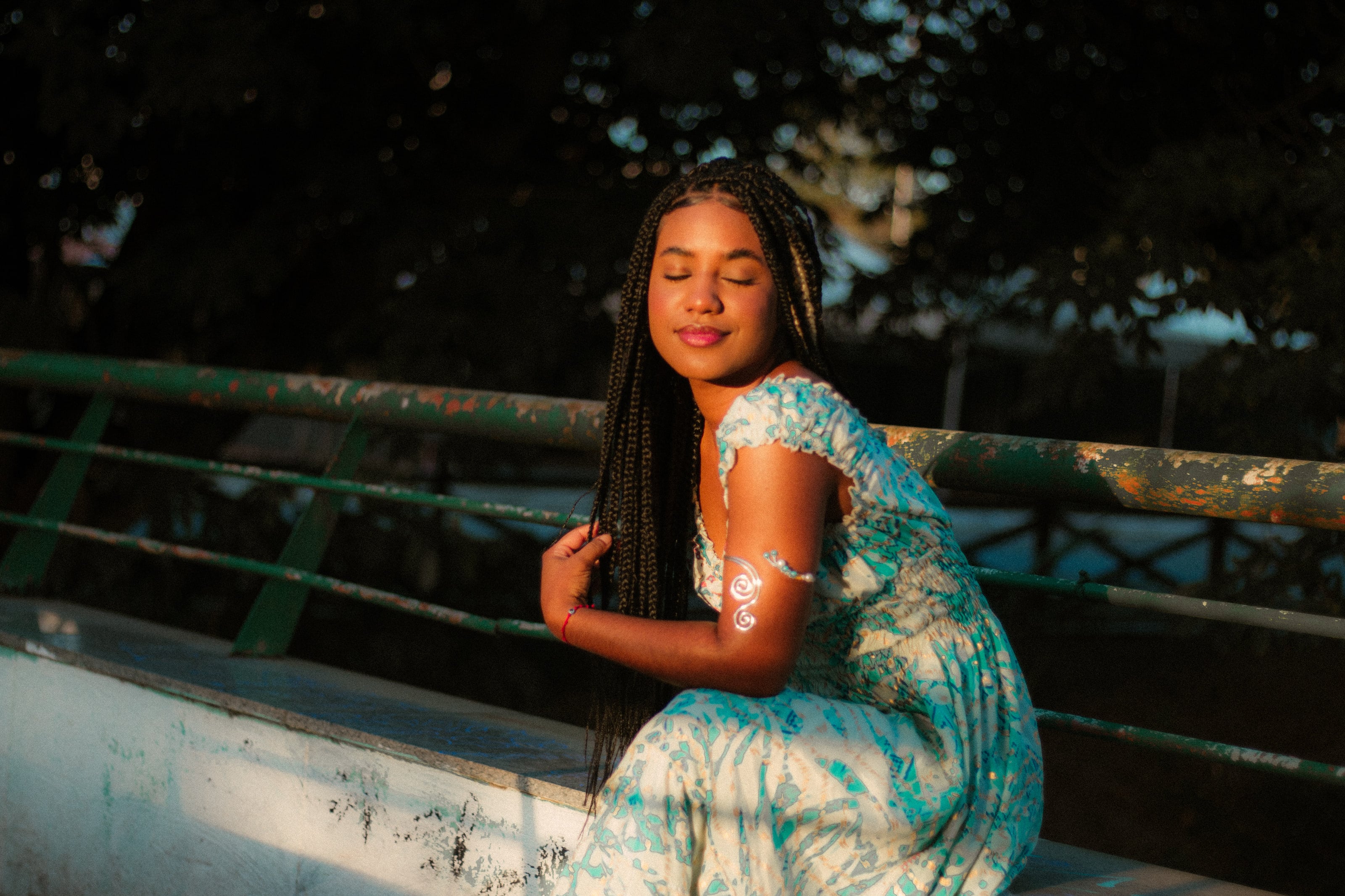 Sentada na mureta de grade verde, na luz de fim de tarde, ensaio individual