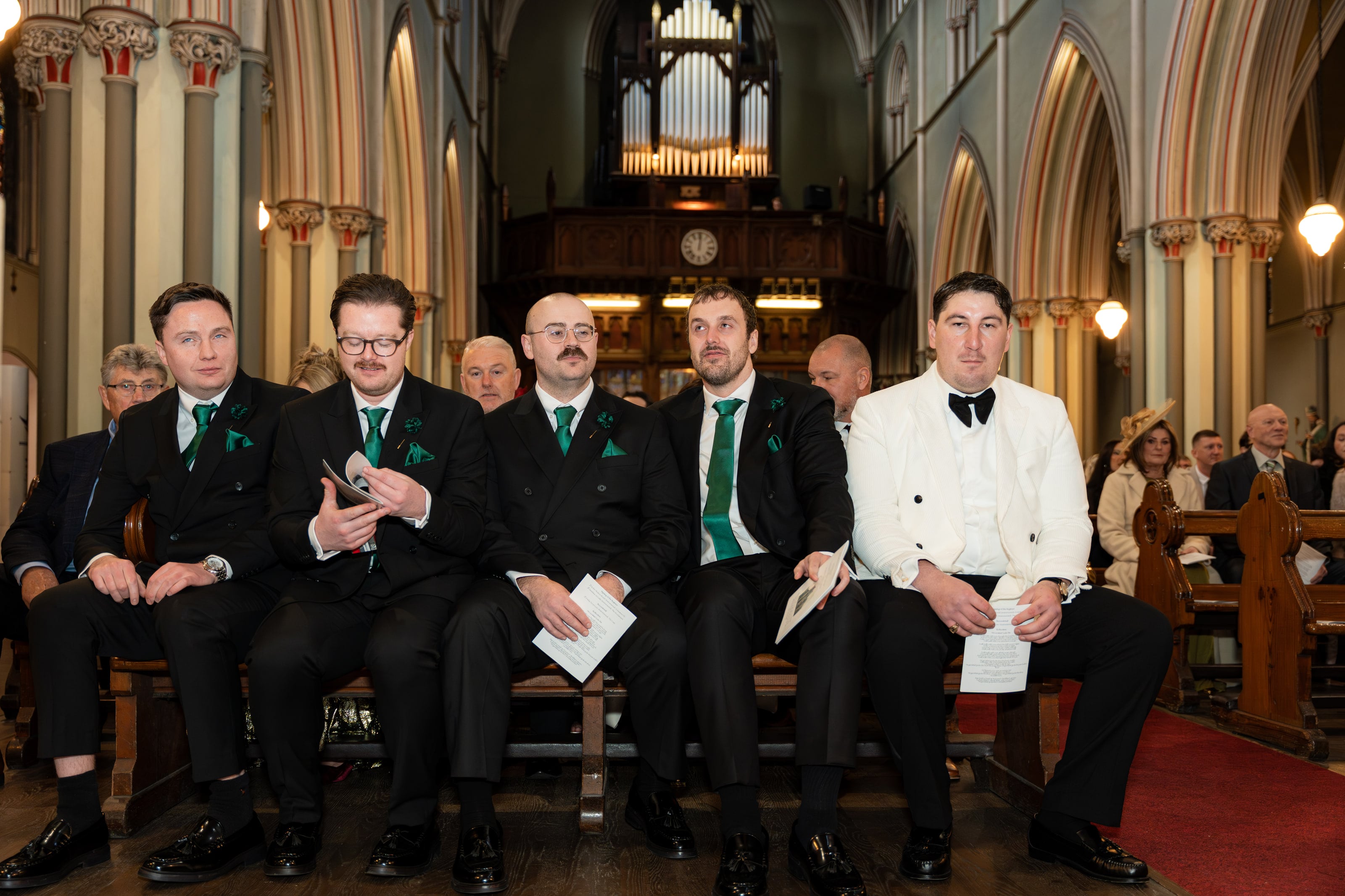 Padrinhos de gravata verde sentados no primeiro banco, casamento de C & S