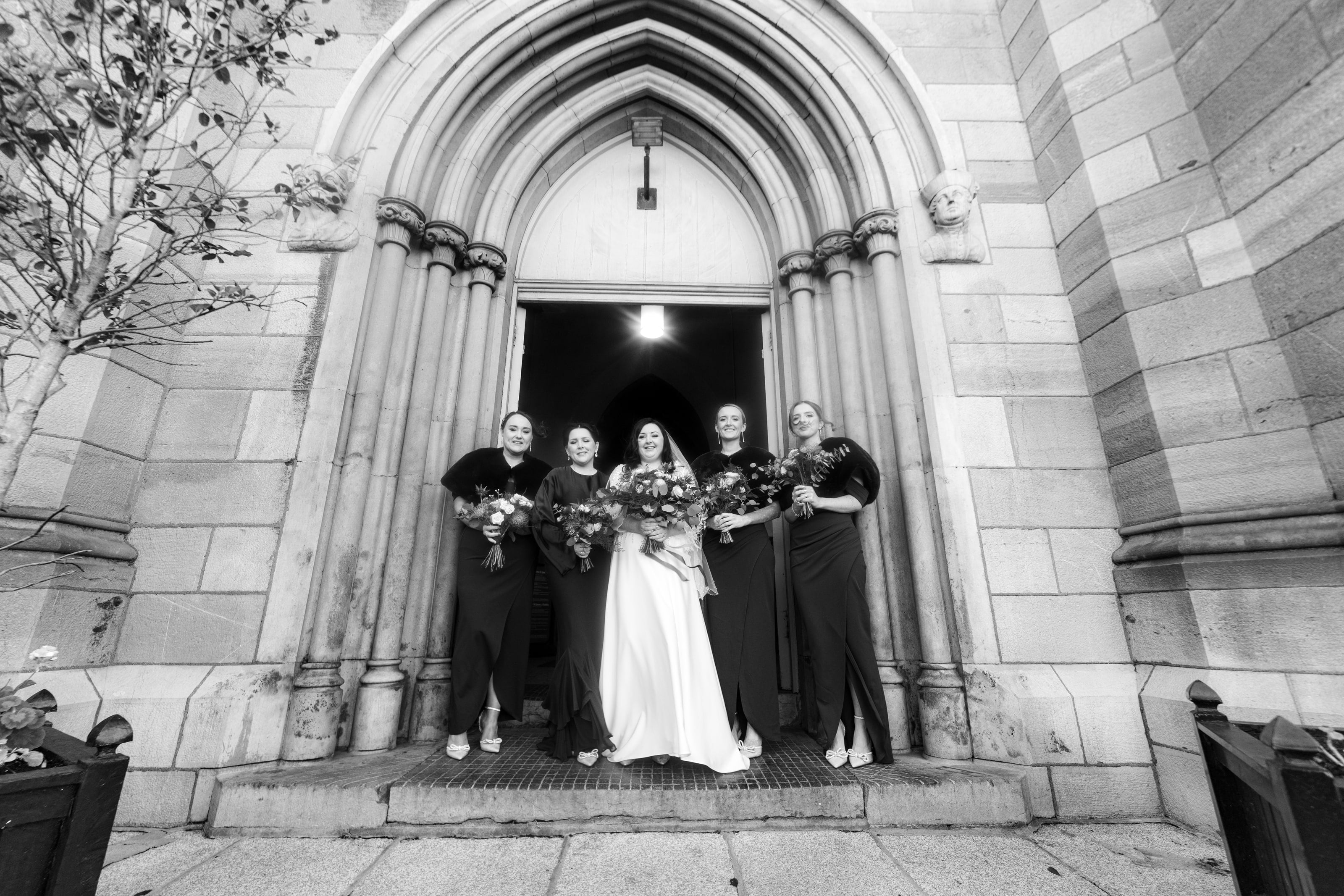 Noiva e madrinhas de preto na porta da igreja, em preto e branco, casamento de C & S