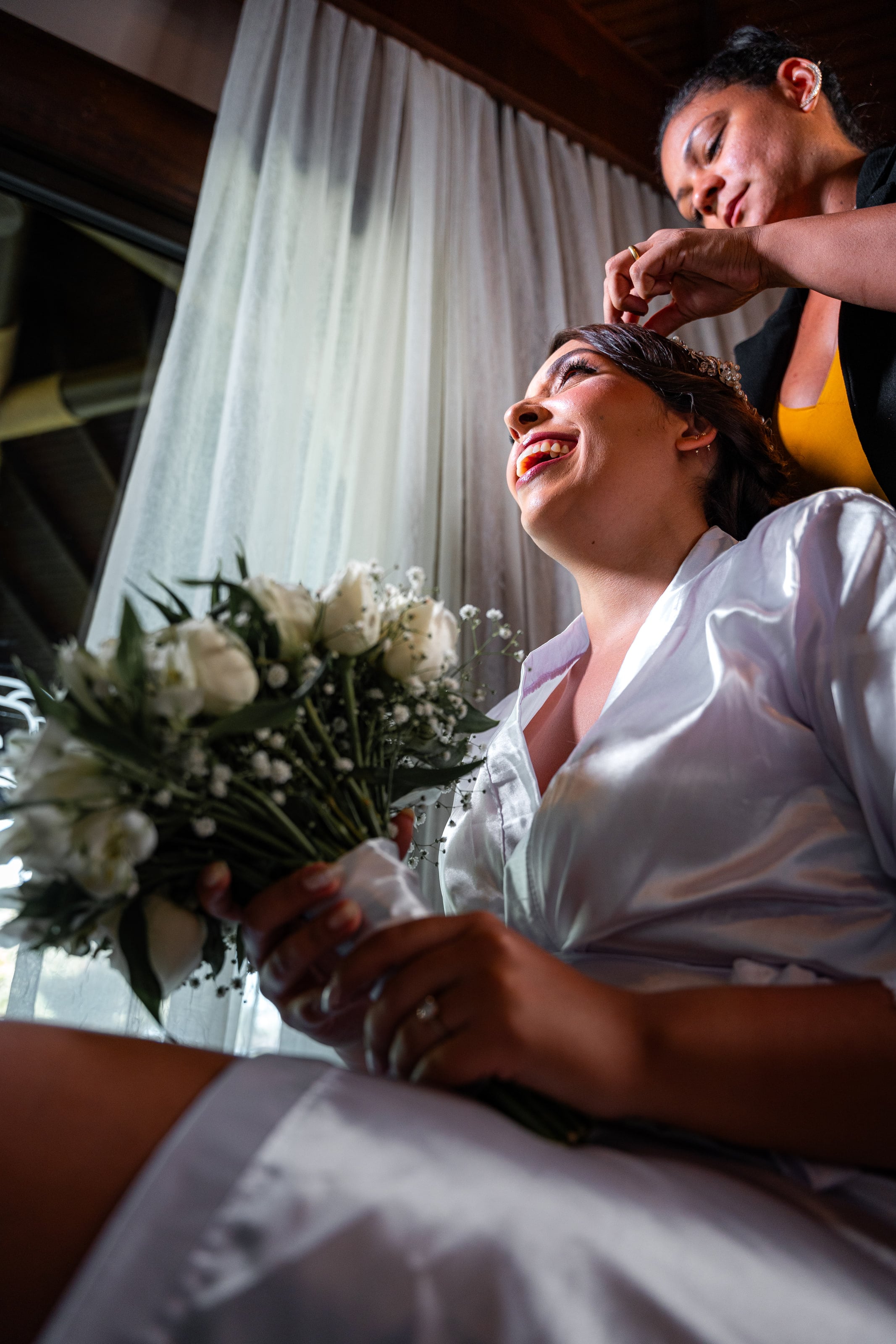 Noiva segurando o buquê de rosas brancas enquanto ajeitam o penteado, casamento de D & S
