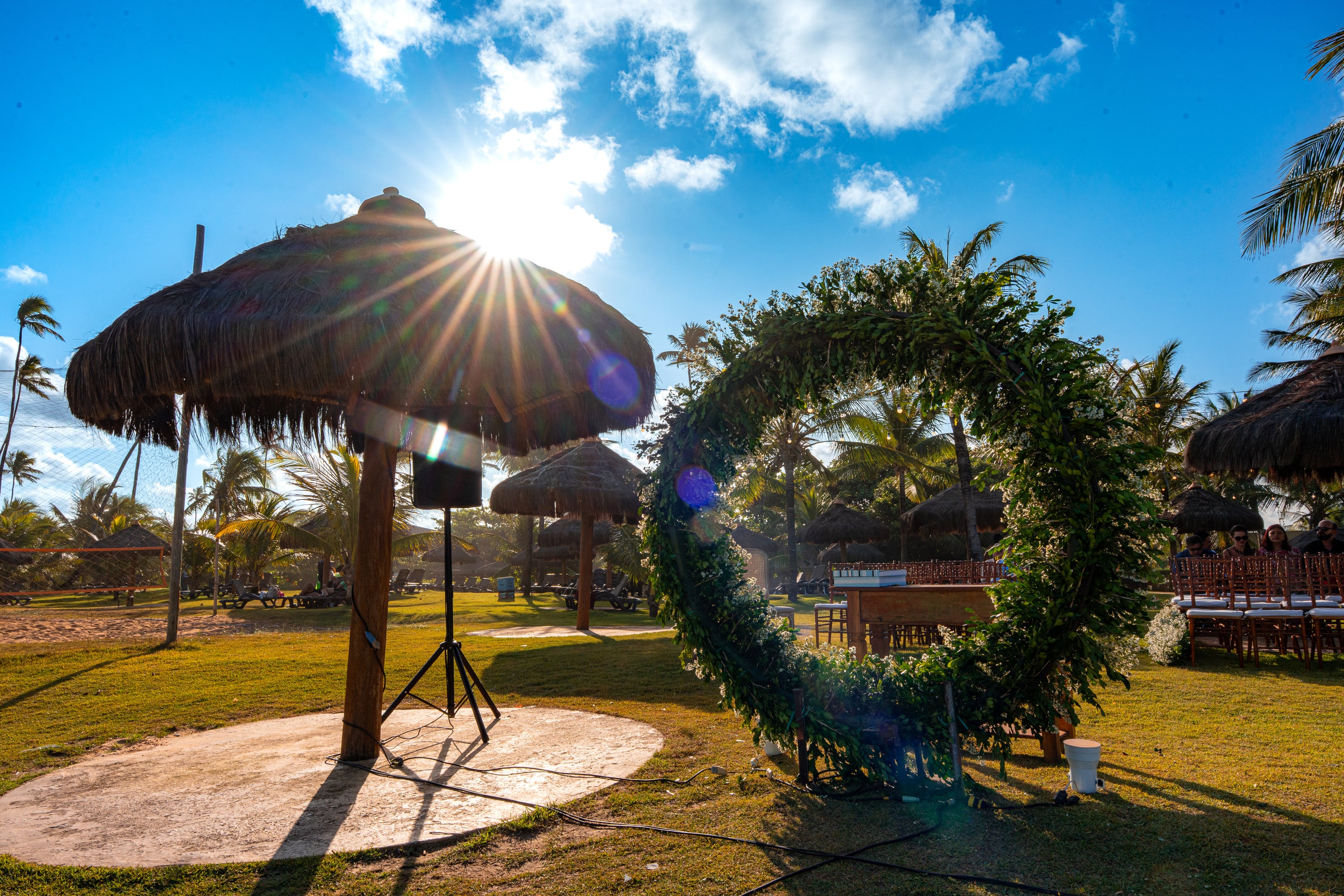 Arco de flores redondo no gramado, ao lado de guarda-sóis de palha, casamento de D & S