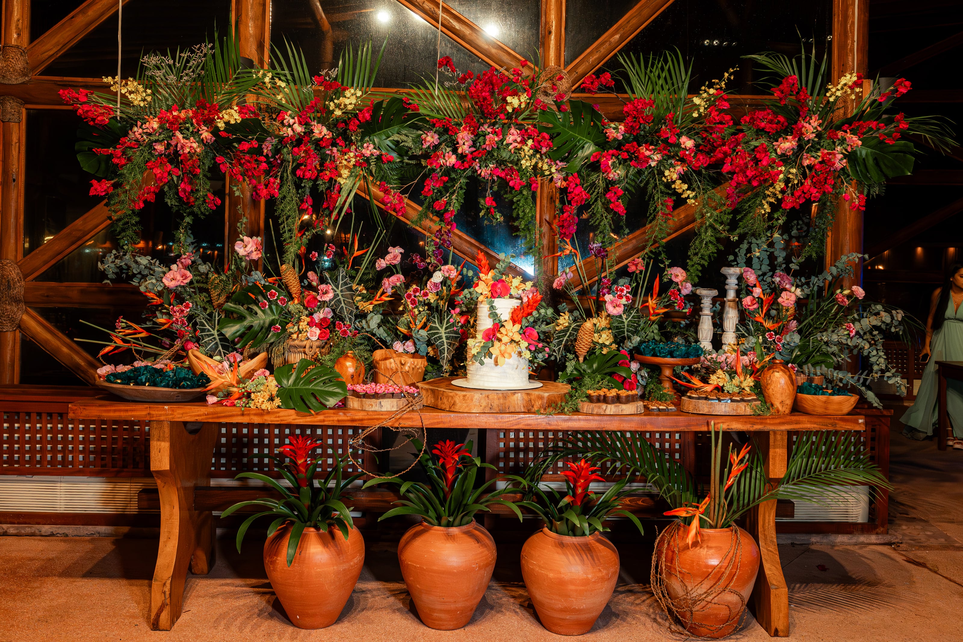 Mesa de doces com flores tropicais vermelhas e vasos de barro, casamento de J & K