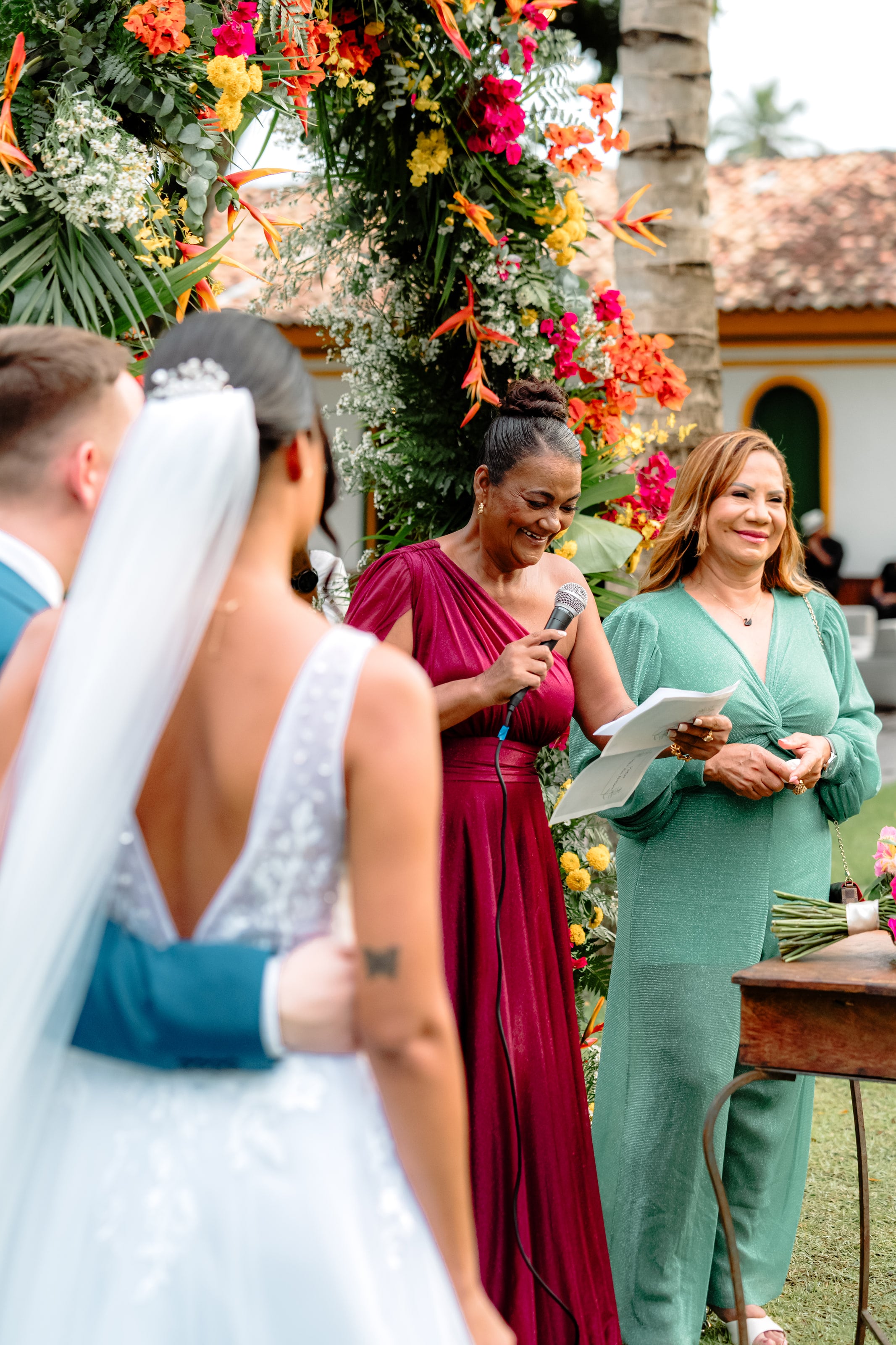 Duas mulheres leem para o casal junto ao arco de flores, casamento de J & K