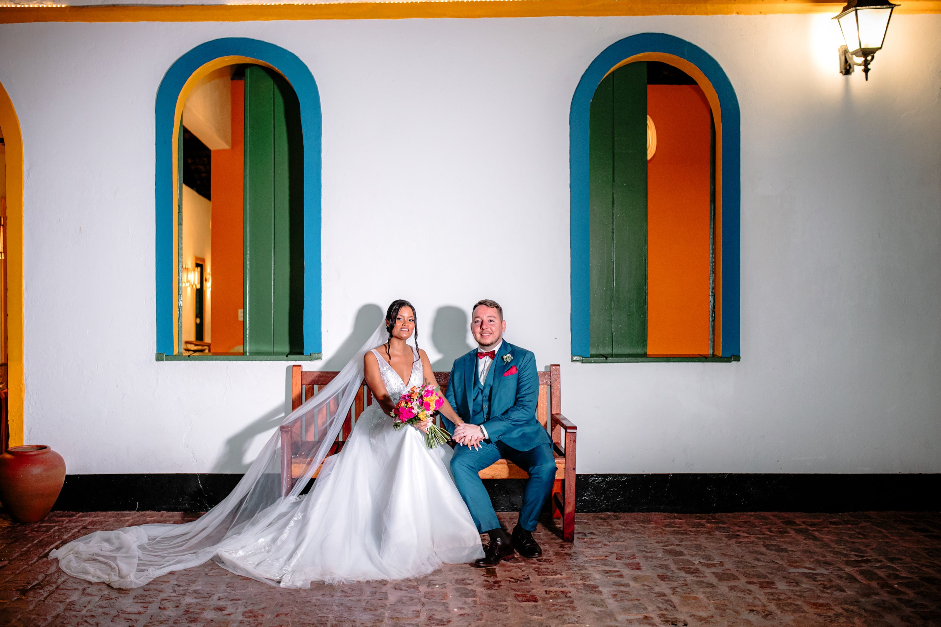 Casal sentado diante do casarão, véu estendido no piso de tijolo, casamento de J & K