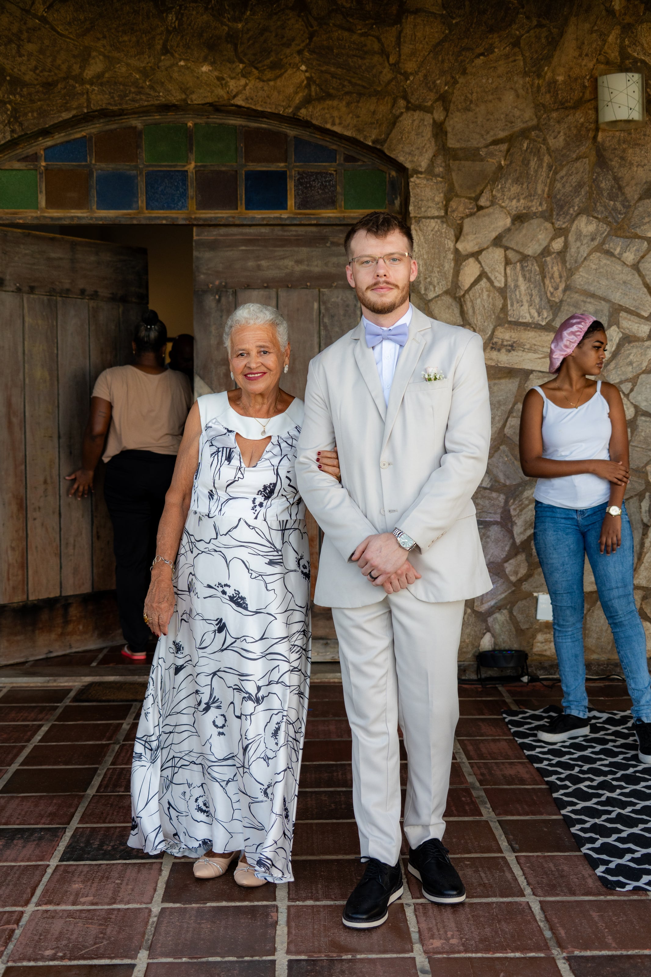 Noivo de terno claro de braço dado com uma senhora na porta de madeira, casamento de L & M em Salvador