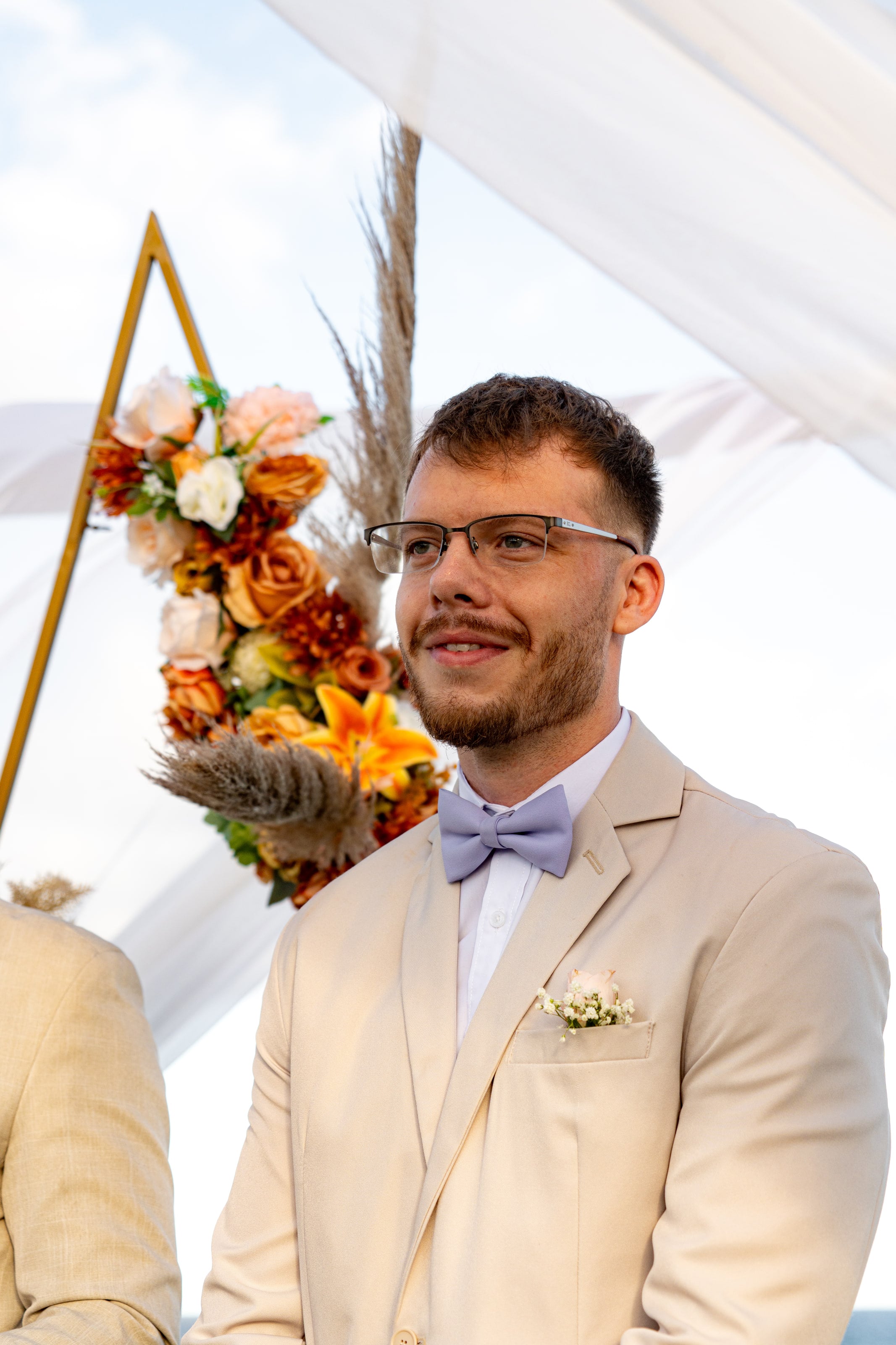 Noivo sorrindo no altar, diante do arco de flores laranja, casamento de L & M em Salvador