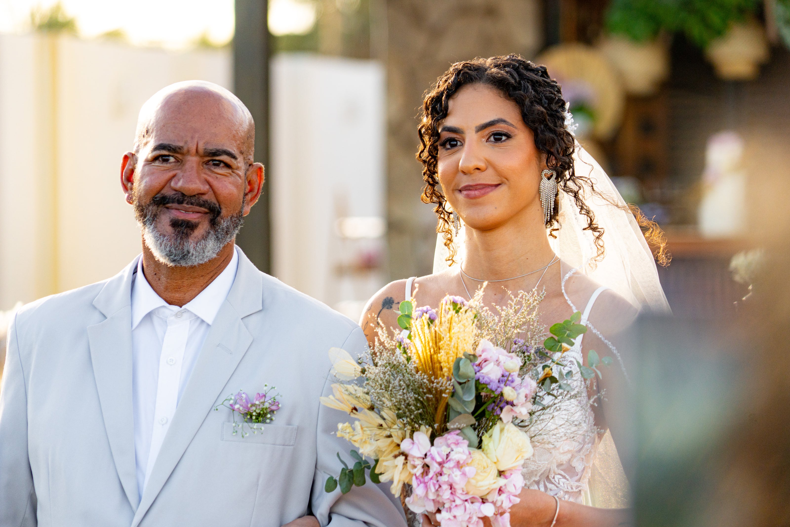 Noiva chegando de braço dado, com buquê de flores do campo, casamento de L & M em Salvador