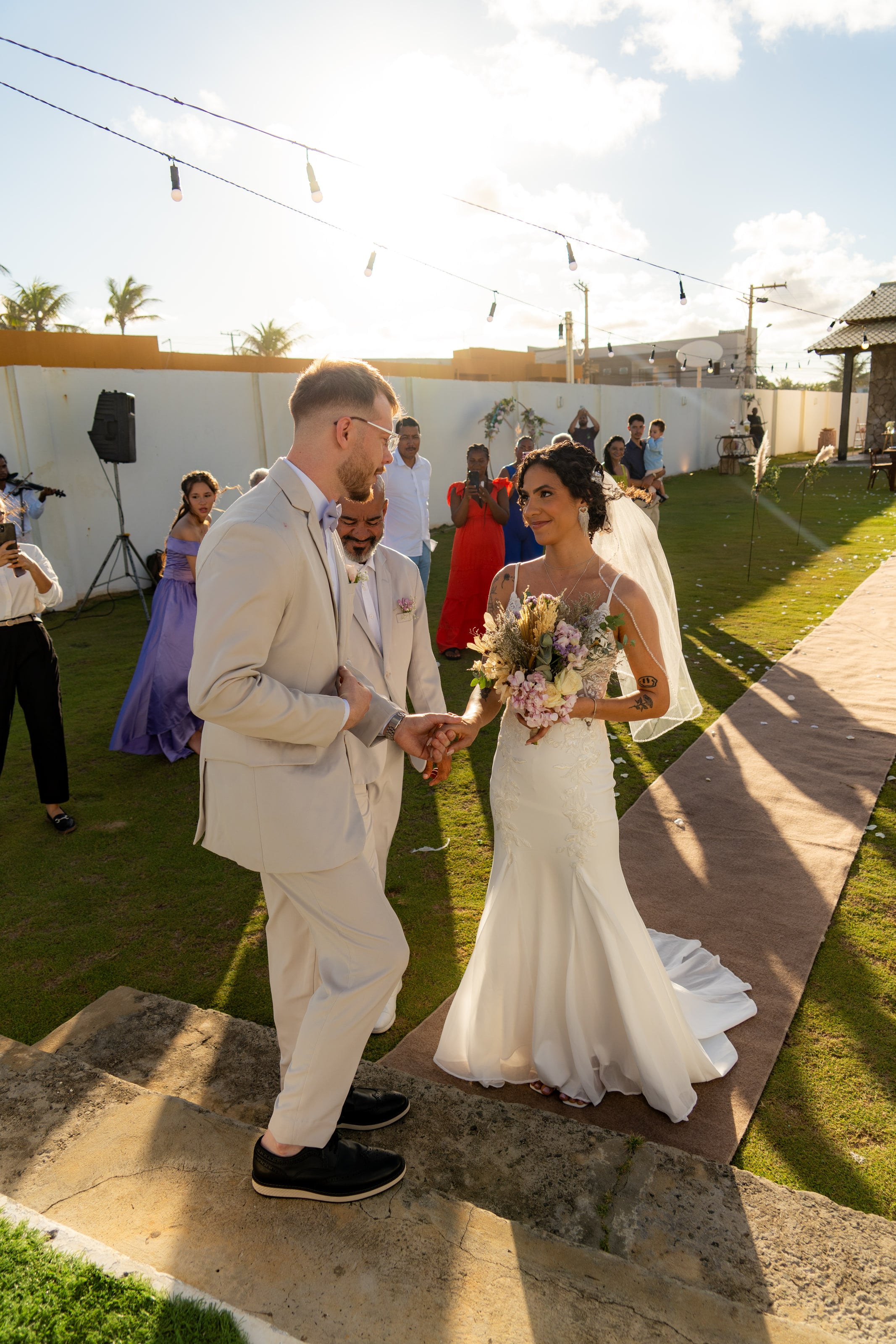 Entrega da noiva ao noivo no gramado, com convidados em volta, casamento de L & M em Salvador