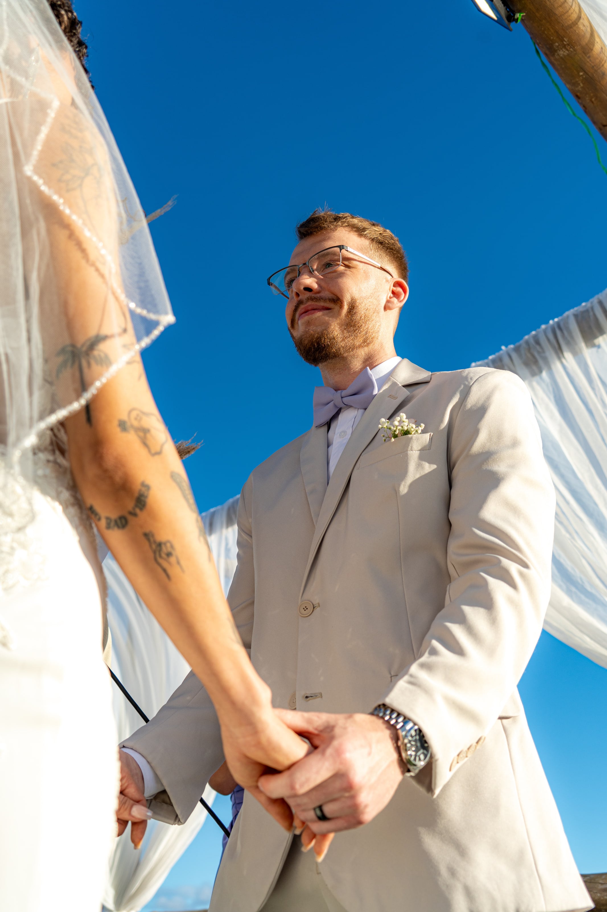 Mãos dadas no altar sob o céu azul, vistas de baixo, casamento de L & M em Salvador