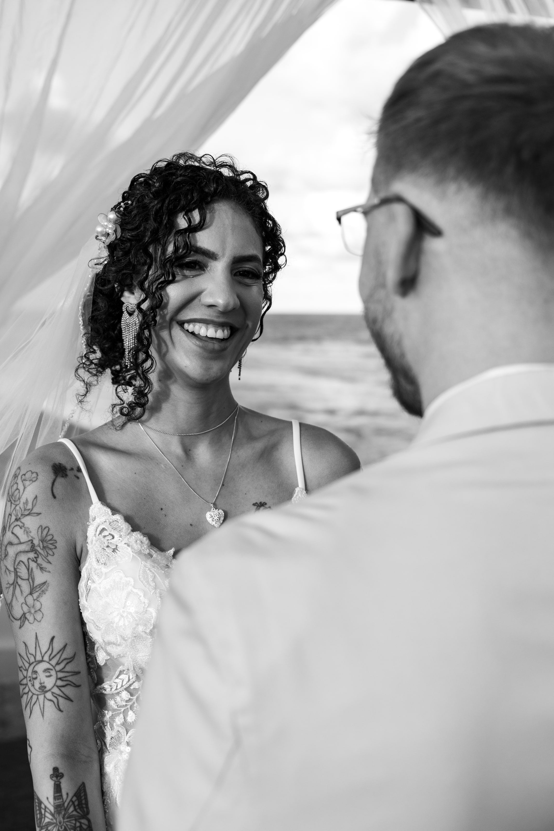 Noiva sorrindo para o noivo com o mar ao fundo, em preto e branco, casamento de L & M em Salvador