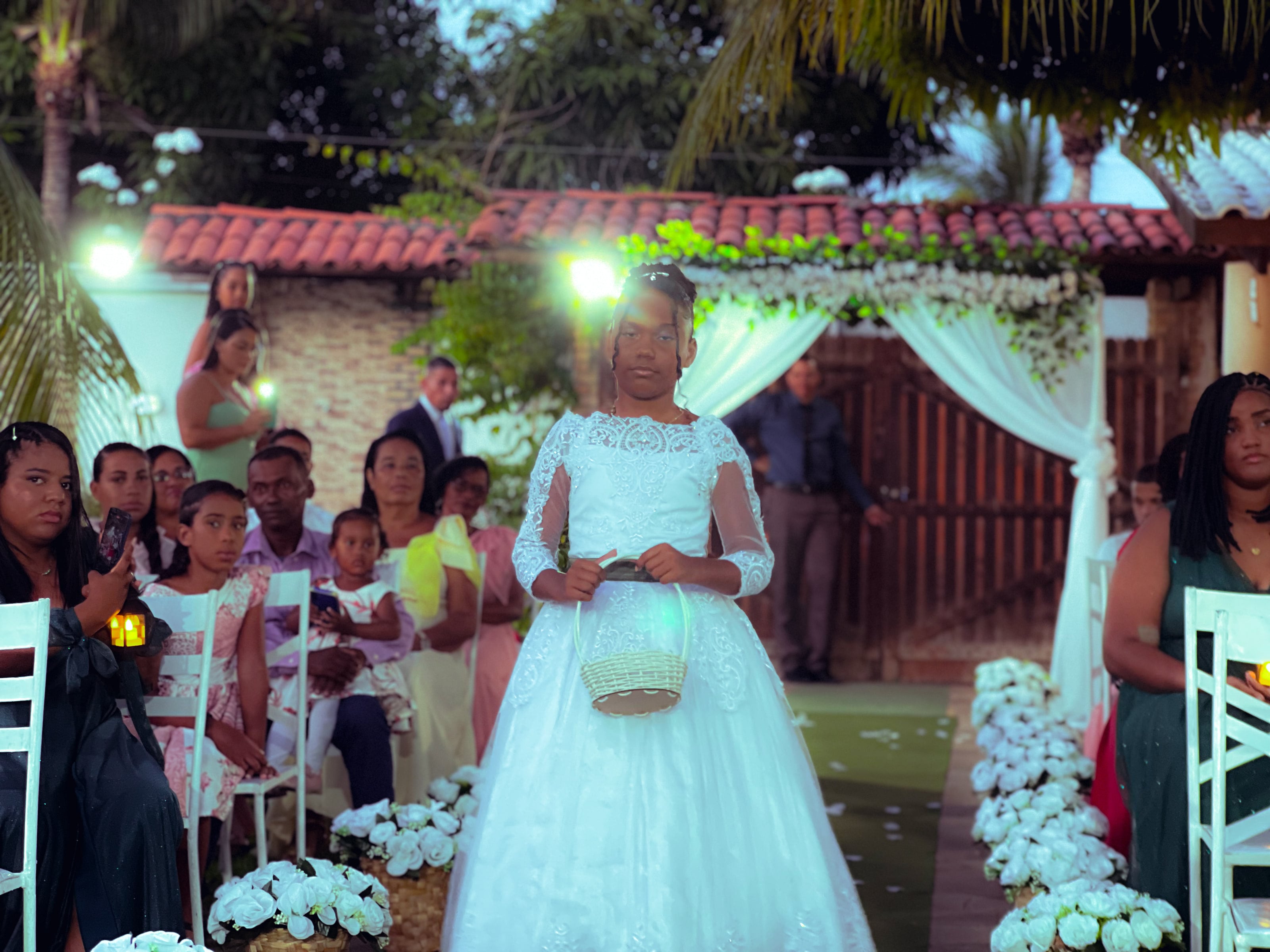 Daminha de vestido branco com cesta de pétalas no corredor, casamento de M & I