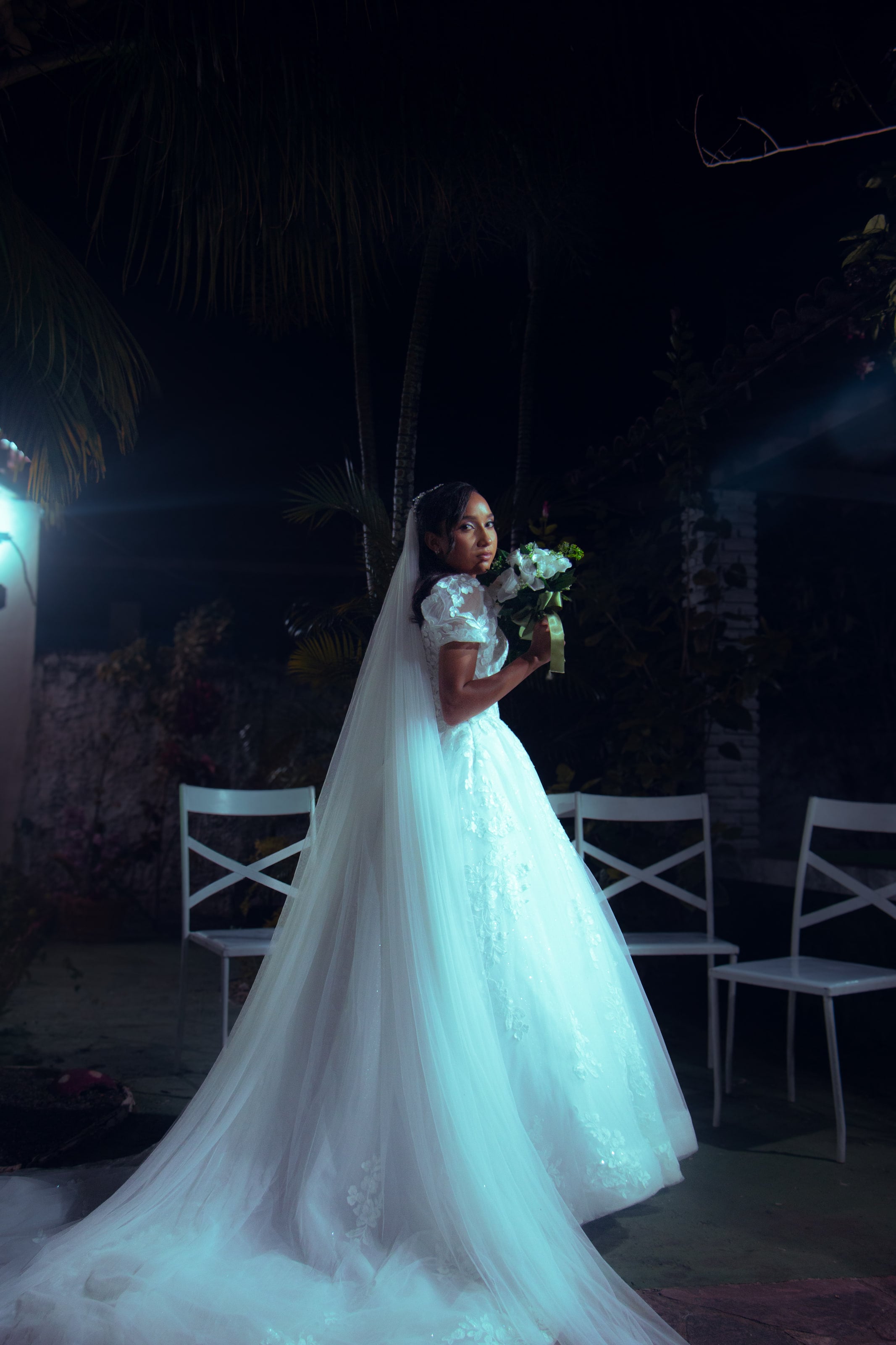 Noiva com o véu longo e o buquê no jardim à noite, casamento de M & I