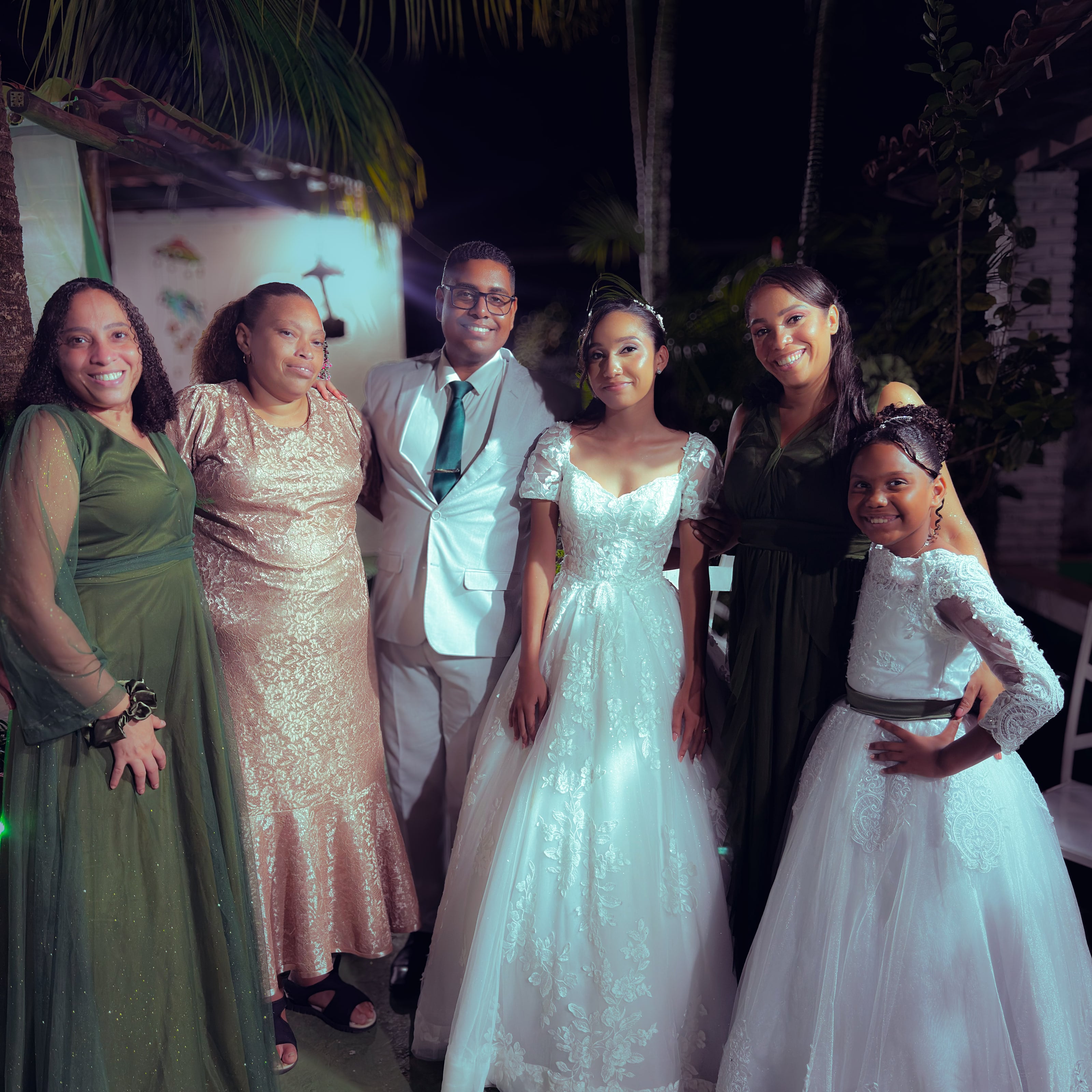 Noiva e noivo com convidados no jardim, à noite, casamento de M & I
