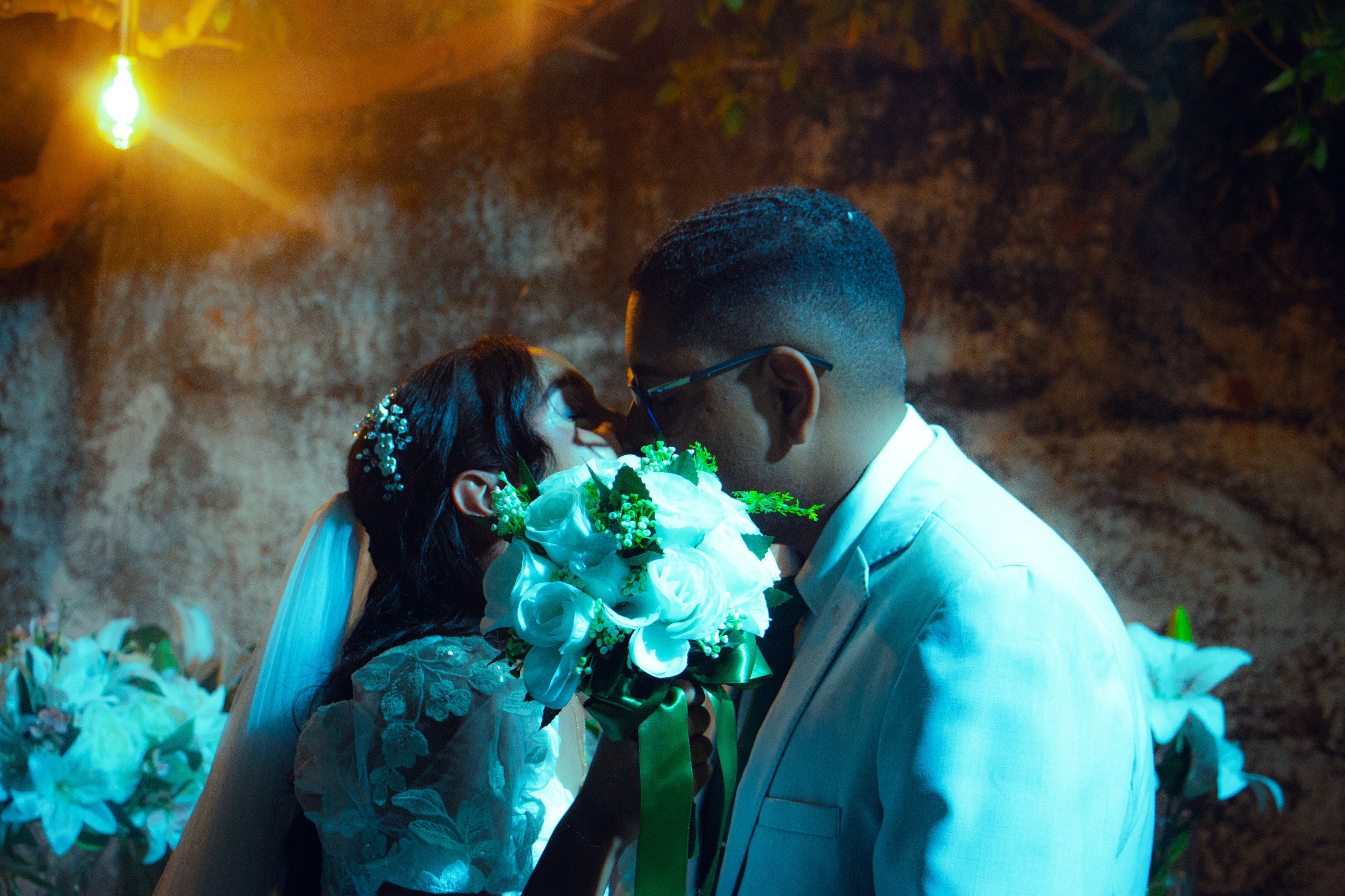 Casal junto à mesa do bolo, sob luzes quentes, casamento de M & I