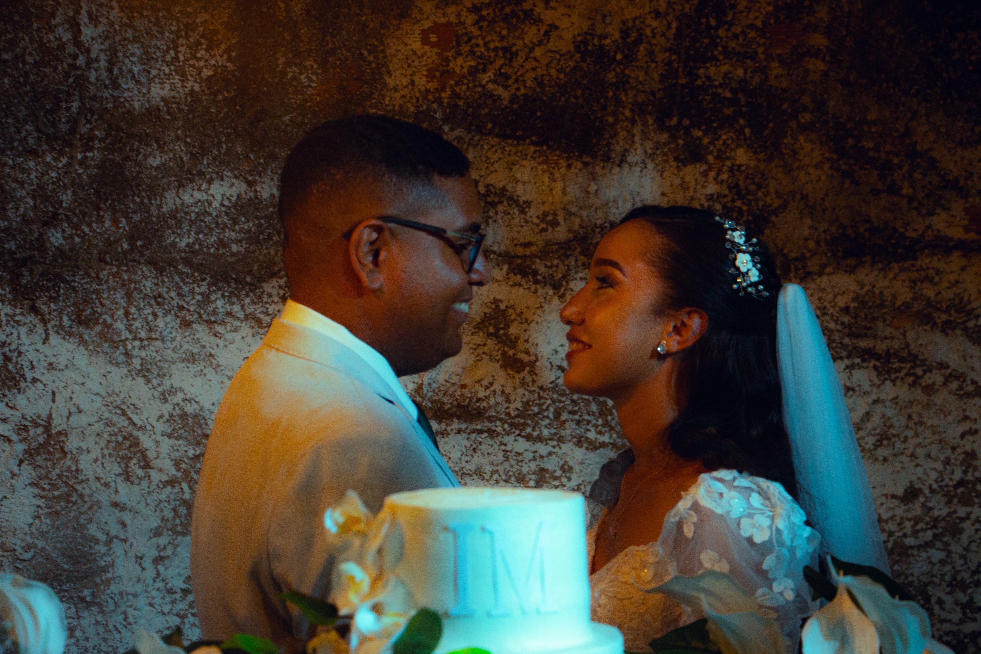 Casal junto à mesa do bolo, sob luzes quentes, casamento de M & I