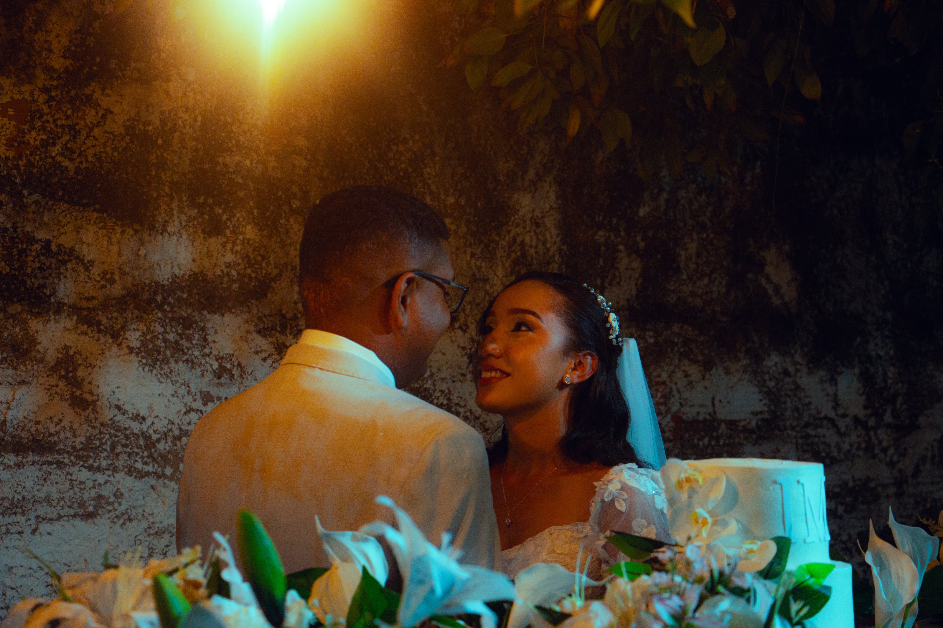 Casal junto à mesa do bolo, sob luzes quentes, casamento de M & I