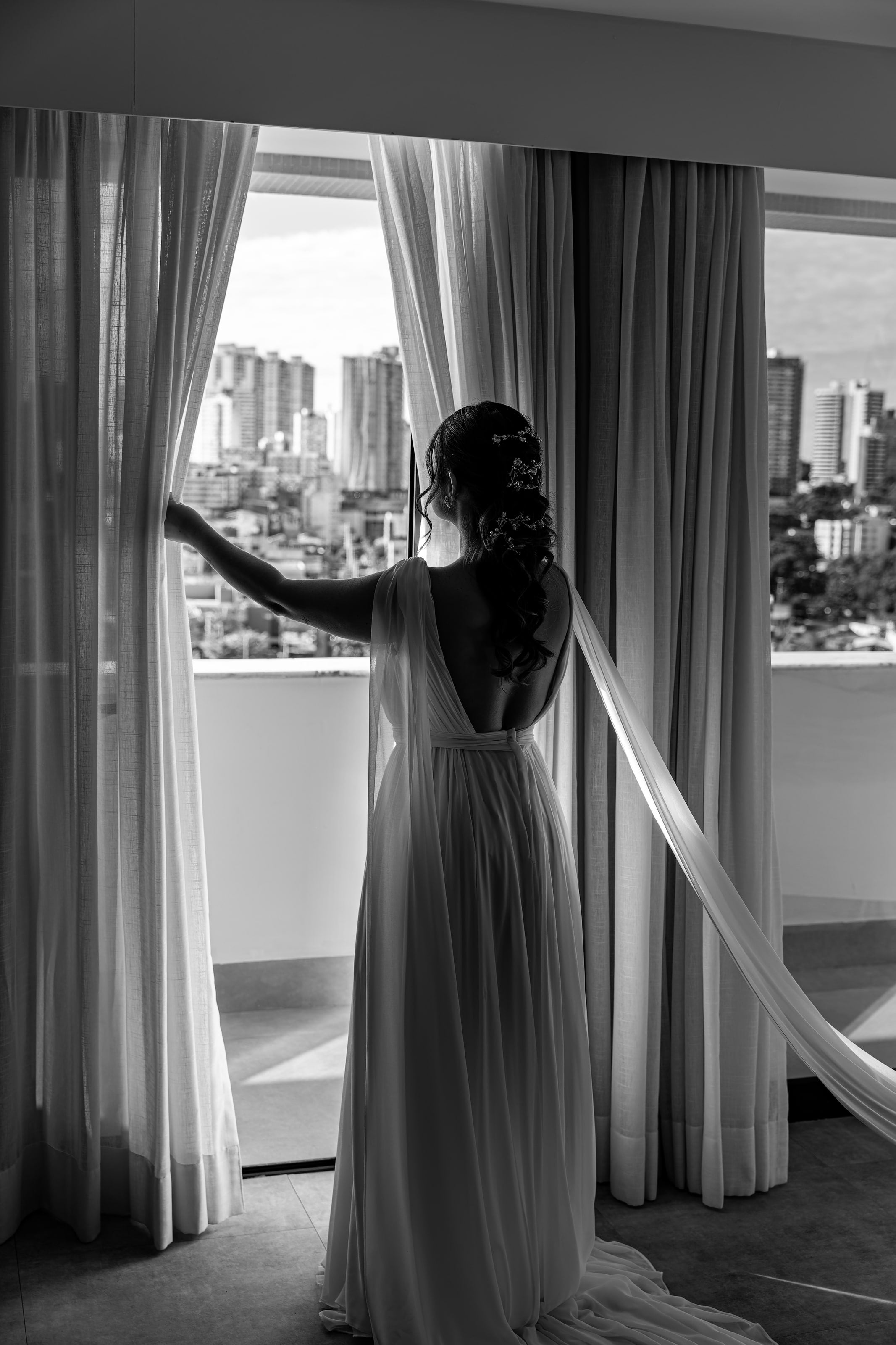 Noiva pronta na janela com vista para a cidade, em preto e branco, casamento de N & H