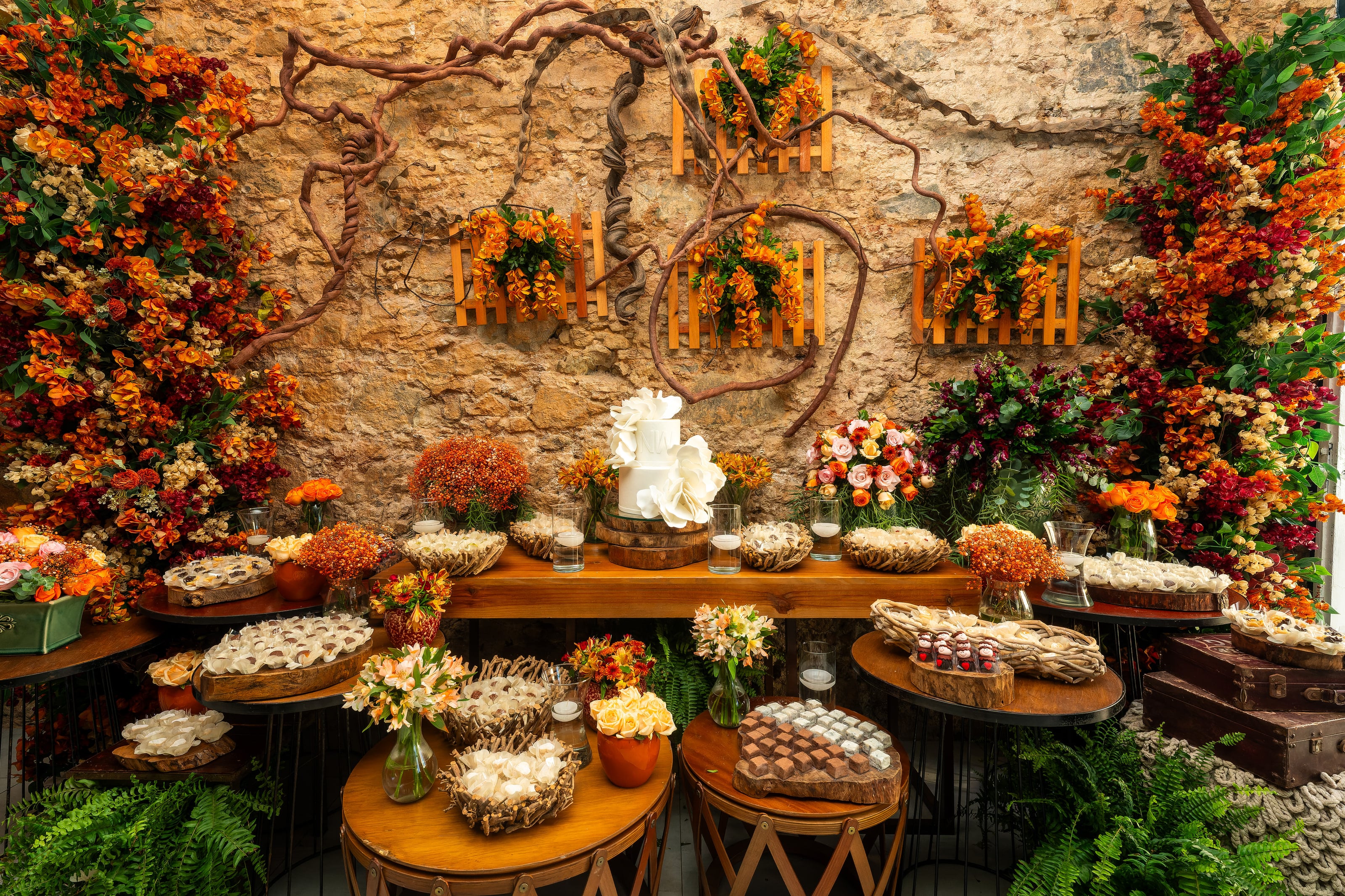 Mesa de doces com flores laranja contra a parede de pedra, casamento de N & H
