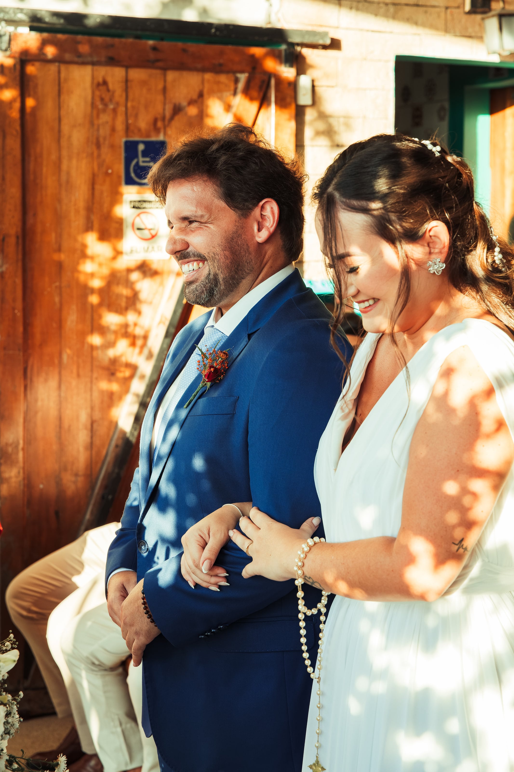 Entrada do casal de braços dados, com o sol entre as folhas, casamento de N & H