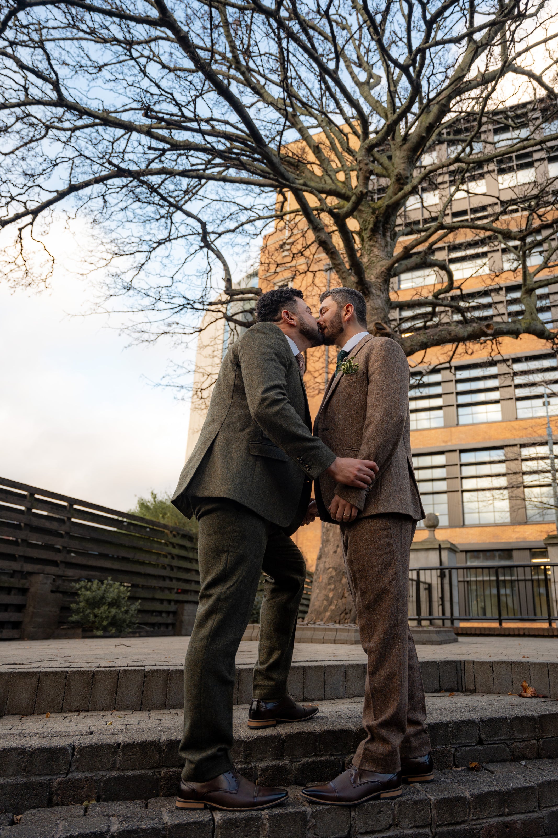 Os noivos se beijam na escada, sob uma árvore sem folhas, casamento de W & F
