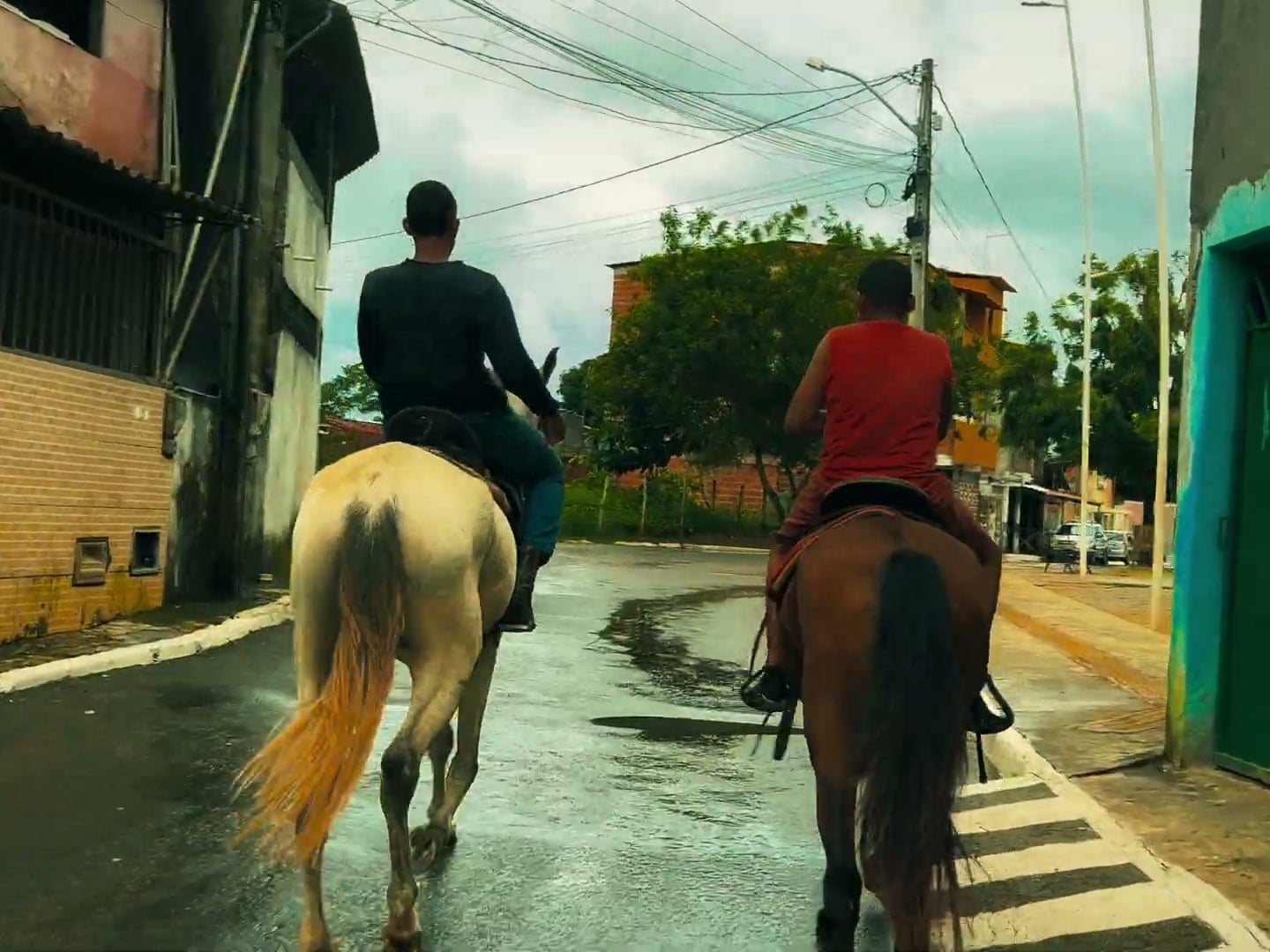 Dois adolescentes se abraçam no meio de uma rua estreita, sob sol forte.