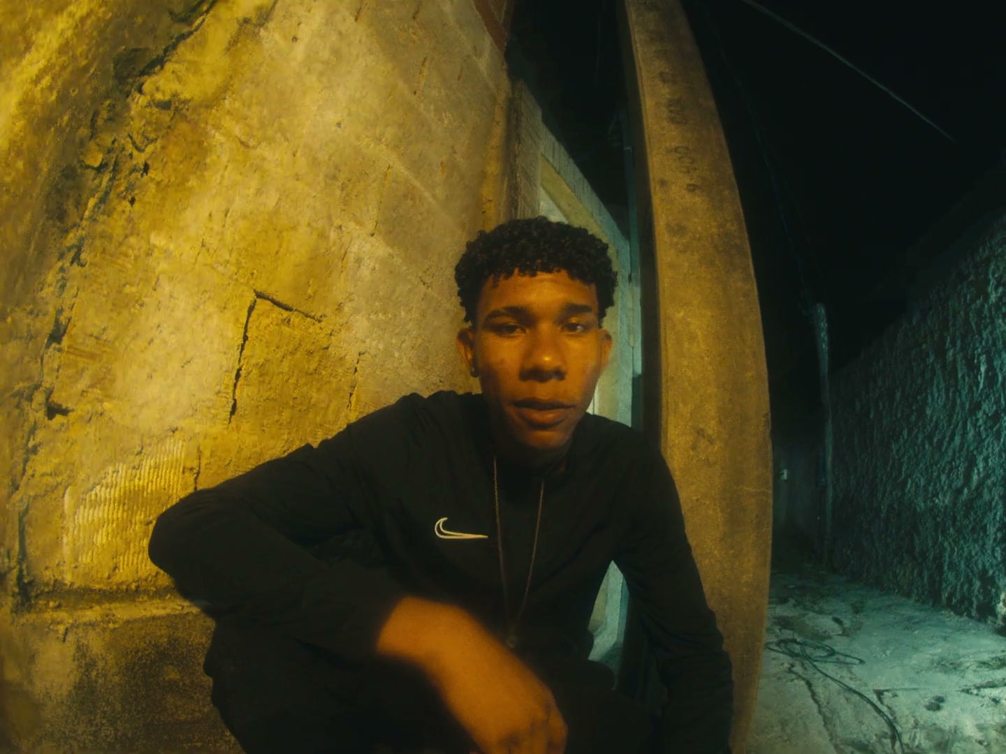 Rapaz sentado diante de uma parede em arco iluminada de dourado, à noite.