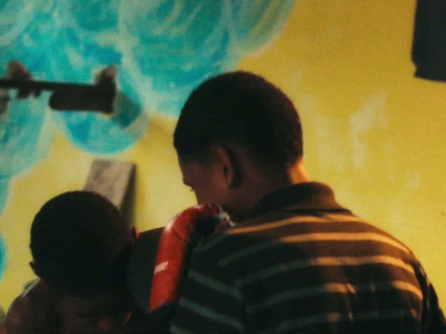 Dois meninos treinam boxe com luvas diante de uma parede amarela com pintura azul.