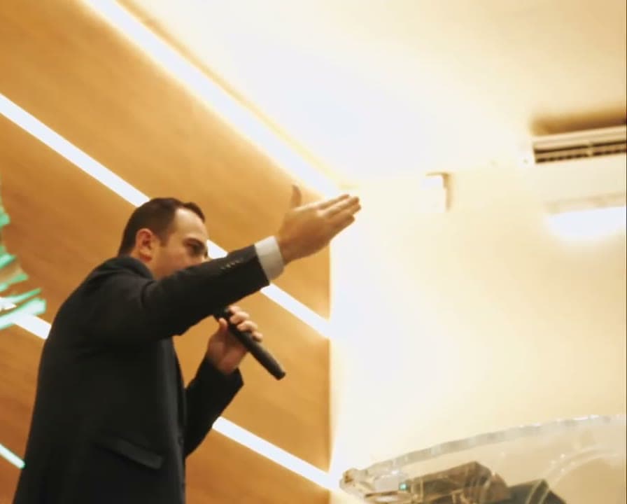 Palestrante de terno com o braço erguido, congresso de jovens filmado pela Duat