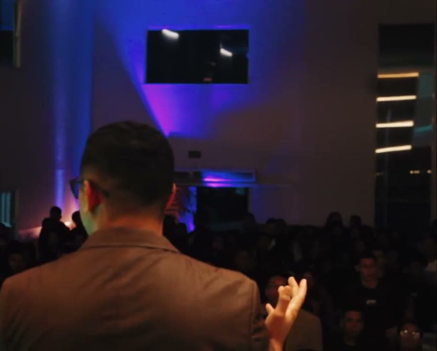 Pregador de costas diante do público, com luz azul no palco, congresso de jovens filmado pela Duat